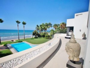Magnifique image du bord de la mer vue d'une terrasse en Espagne. On voit une piscine scintillante et des palmiers.