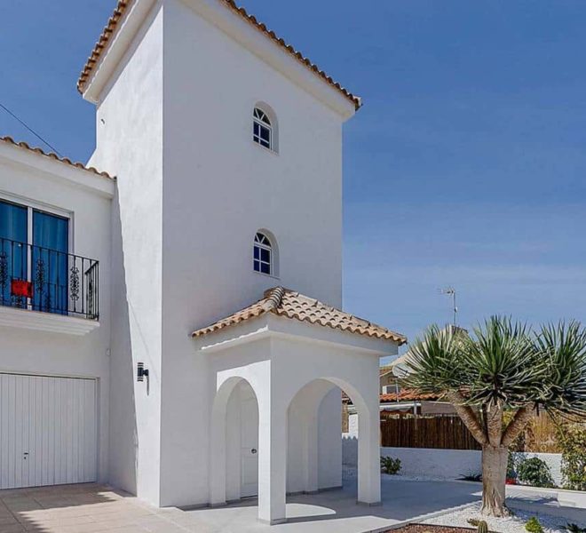 Image d'une villa indépendante de style méditerranéen située à Torrevieja. On peut voir l'entrée du garage à véhicule et un palmier.